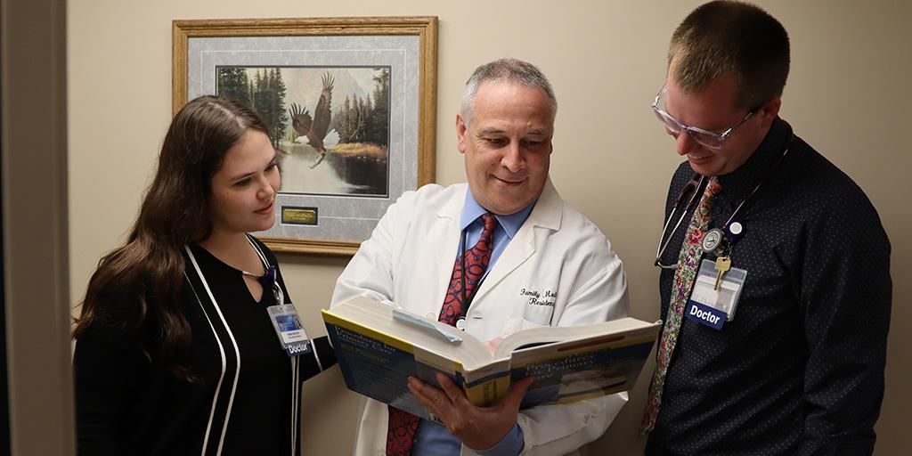 Doctor holding textbook while two residents look on.