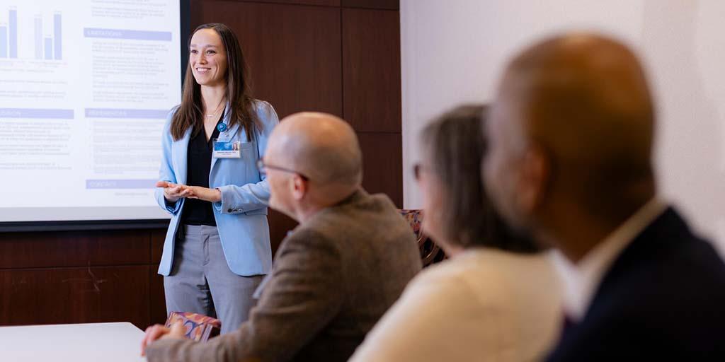A General Internal Medicine (GIM) fellow gives a presentation to the rest of her cohort in a conference room.