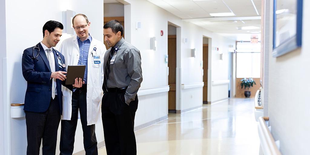 Three doctors stand in the hallway having a discussion while looking at a digital tablet.