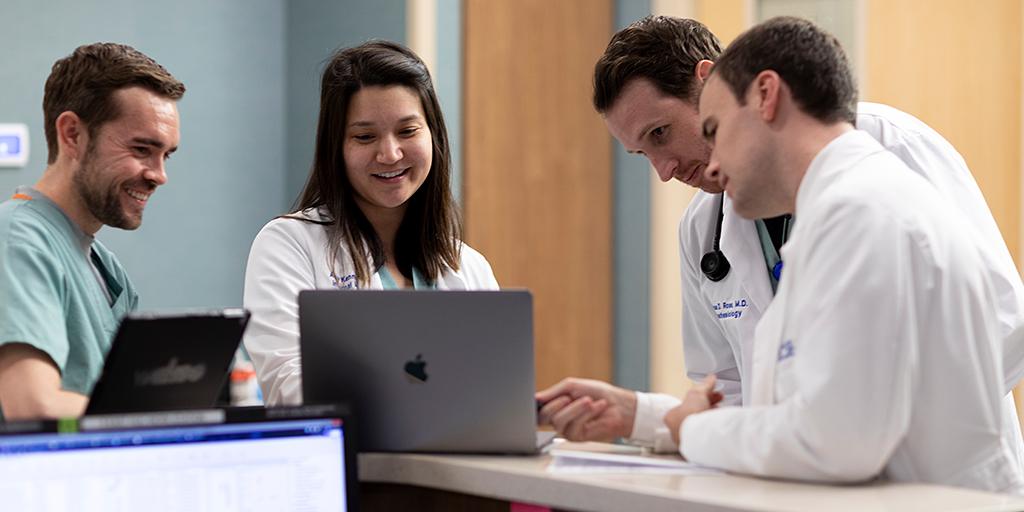 Internal medicine residents gather around a laptop to discuss a case. 