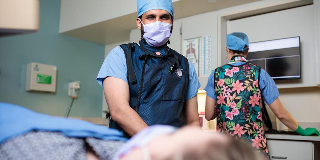 In an examination room, a doctor interacts with a patient while a medical staff member assist in the background.