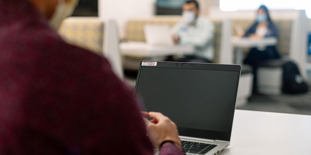 Looking over the shoulder of a student who is on his laptop in a study area.
