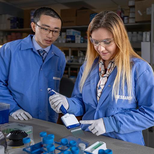 Harry Min, PhD, and Stephanie Oatman, PhD, Research Fellows, collaborating in the research lab using a multichannel pipette.
