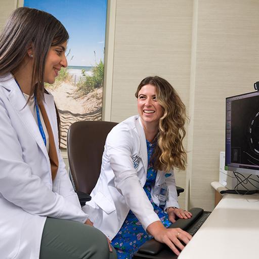 A Hematology/Oncology Physician Assistant and an Advanced Practice Providers (APP) fellow review a computed tomography (CT) imaging scan on a computer in an office together
