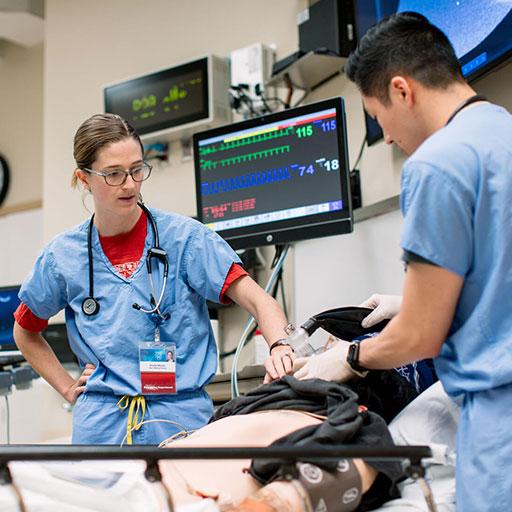 Photo of three NPs or PAs in an emergency room setting, surrounded by vital screens and looking at patient in hospital bed.