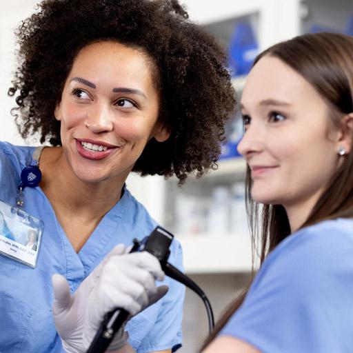 Corinna Hughes, APRN, CNP, DNP, Urology Nurse Practitioner, guides Kelsey Block, MPAS, PA-C, MS, Nurse Practitioner or Physician Assistant (NP/PA) Urology fellow, during a cystoscopy in a procedure room.