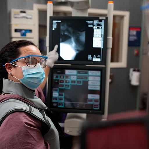 Person wearing mask in an ultrasound room pointing at screen