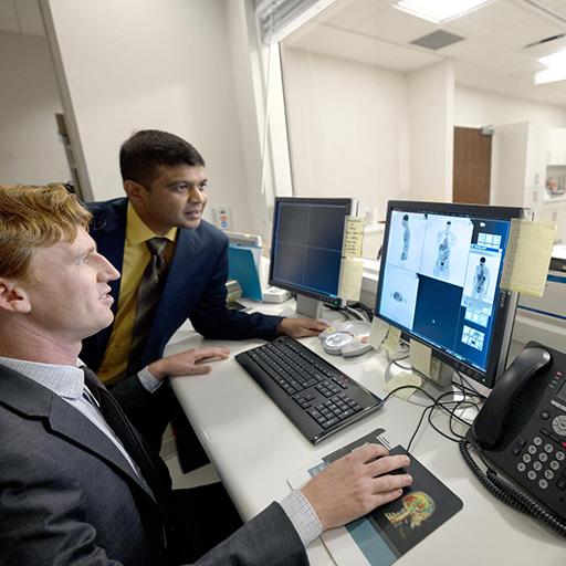 Two people from the Cardiology, Echocardiography Fellowship program at Mayo Clinic in Jacksonville, Florida looked at images on a computer screen while another person was with a patient in the background.