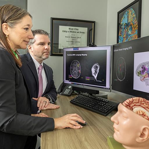 Two doctors look at images from a brain scan on a computer screen.