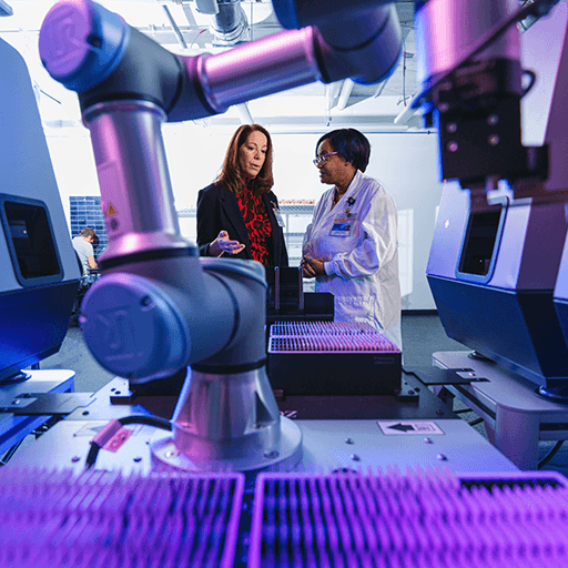 As seen through a robotic arm on an automated digital slide scanner, Annette Bjorheim, Department of Laboratory Medicine and Pathology supervisor, and Jacquese Mitchell, Tissue Registry technician, speak in the Tissue Registry.