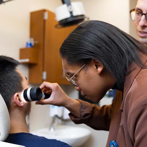 Seneca Hutson, MD, Dermatology resident, uses a dermatoscope while examining a practice patient in an exam room.