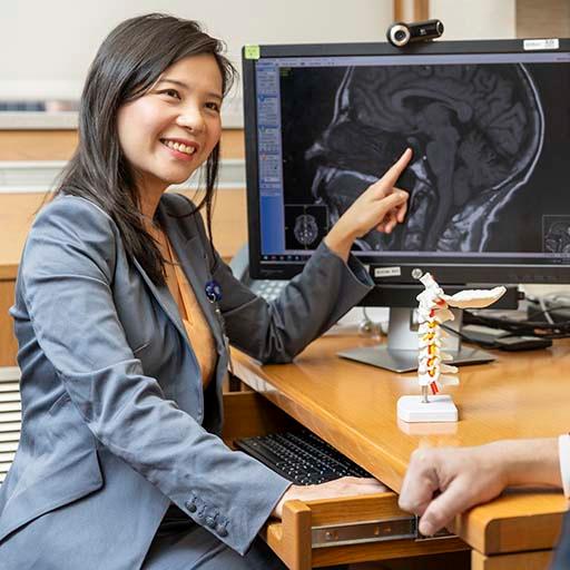 A neurology consultant points to medical imaging of the brain while talking with a patient in an office.