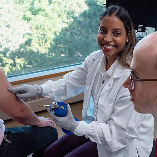 Two internal medicine residents conduct a procedure on a patient arm.