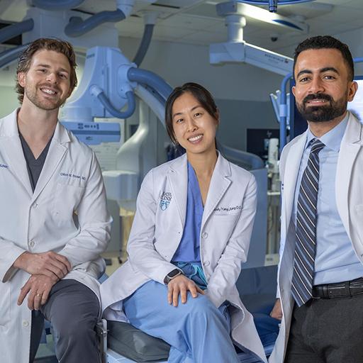 Three doctors pose for a photo inside an operating room.