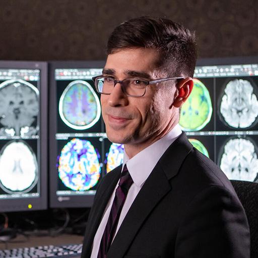 A Mayo Clinic fellow speaks in a reading room where brain scan images are displayed on screens