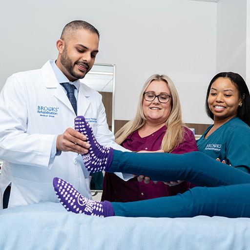 Two staff members observe Dr. Persaud perform a rehabilitation exercise with a patient.