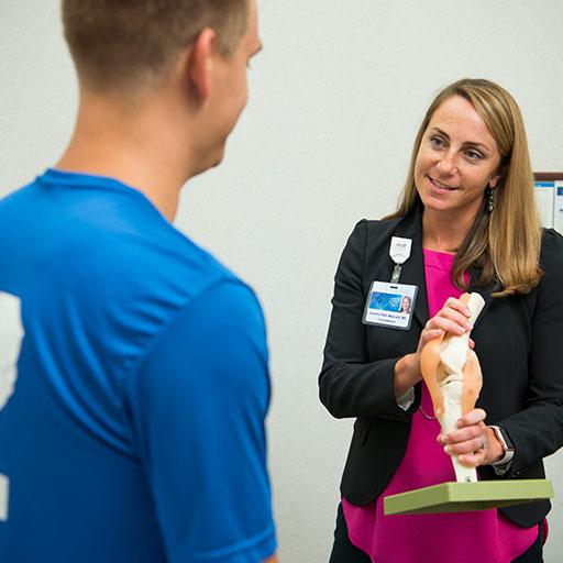 Primary Care Sports Medicine fellow speaking with a patient holding a model.