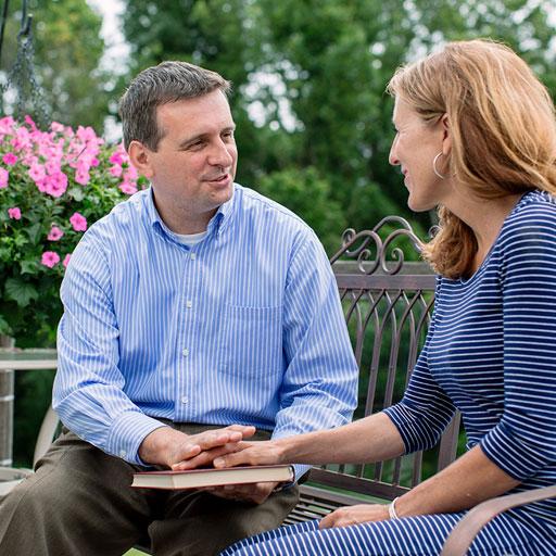 A hospital chaplain sits on a park bench and provides spiritual counseling to a woman