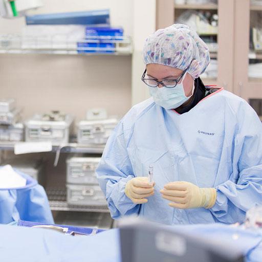 Two nurses wearing surgical scrubs and masks in an operating room evaluating something on an exam table
