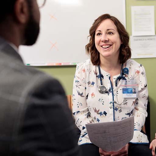 NP sitting in an exam room with two patients and interacting with them about their care