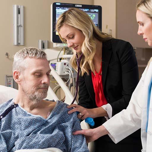 Solid organ transplant physician and fellow meet with a patient in an exam room