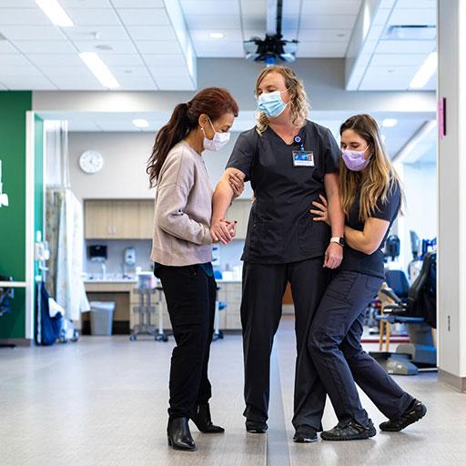 Two physical therapists assisting a patient stand in a health care setting