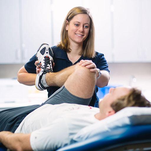 Physical therapy student working with a patient who is on a hospital bench on a leg stretch