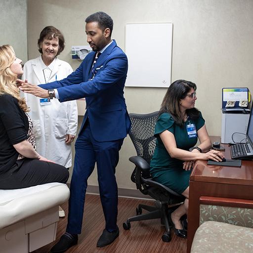 Three doctors consult with a patient in an exam room.