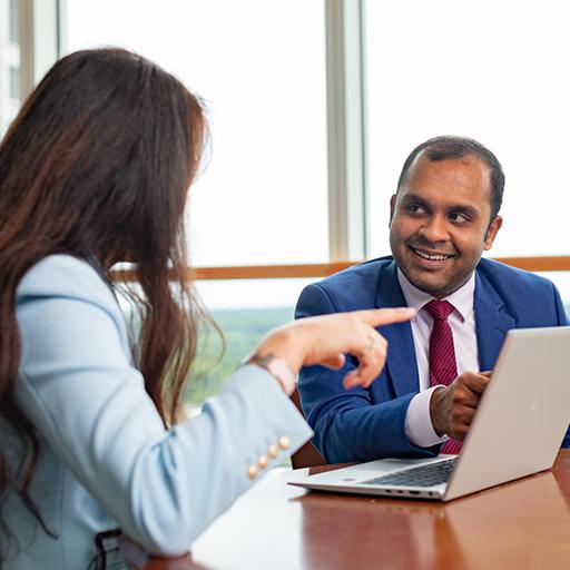 Two doctors in a conference room sitting at a table having a discussion while using a laptop.