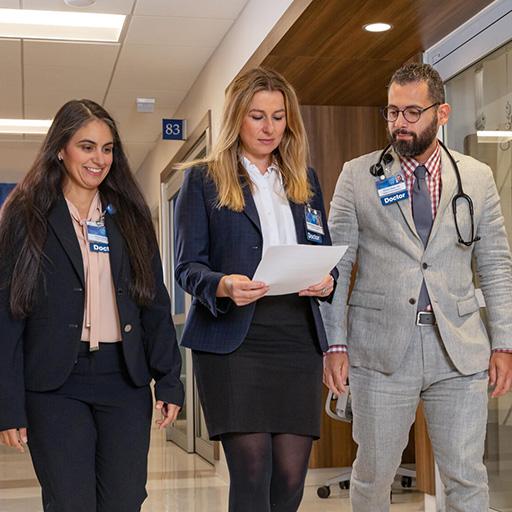 Three Hospital Medicine Fellowship team members converse and review paperwork in a hospital hallway.