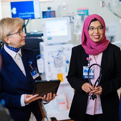 Nephrology fellows and faculty stand together in an inpatient dialysis room, talking and collaborating.