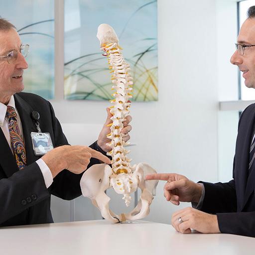Physical Medicine and Rehabilitation Residency doctors observe and discuss an anatomical spine model in a conference room.