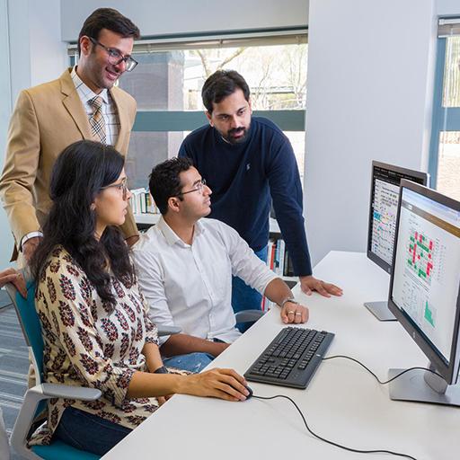 A group of Mayo Clinic and Arizona State University (ASU) students and faculty consult and work together at a computer station. Colorful charts and graphs can be viewed on the computer screen.