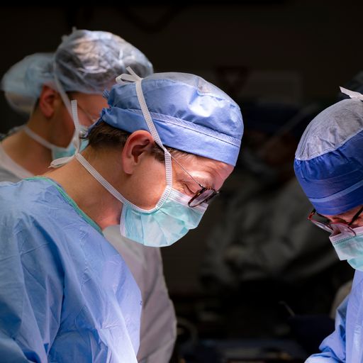 Three doctors are dressed in medical attire and performing a procedure in an operating room.