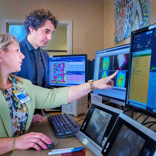 Two doctors in an office looking at five different monitors of patient information and images.