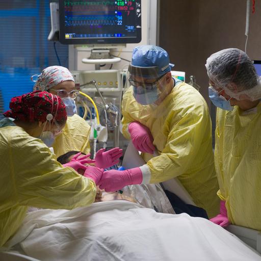 Four intensive care team members in a hospital room work to secure a patient's airway.