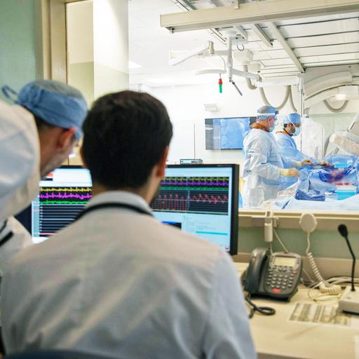In a cath lab, two people watched on as two people performed a procedure on a patient.