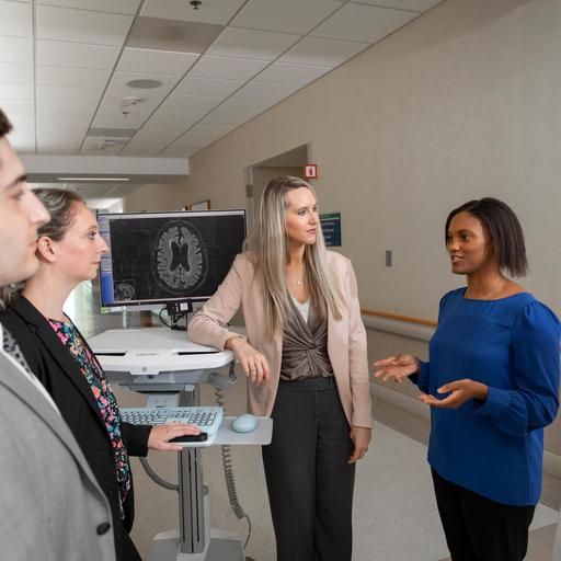 Five people are standing around a computer monitor in the hallway having a discussion.
