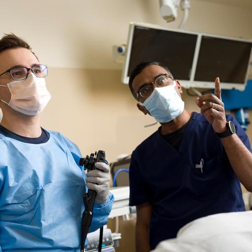 Two people in an exam room standing side by side wearing face masks having a discussion and looking at a monitor.