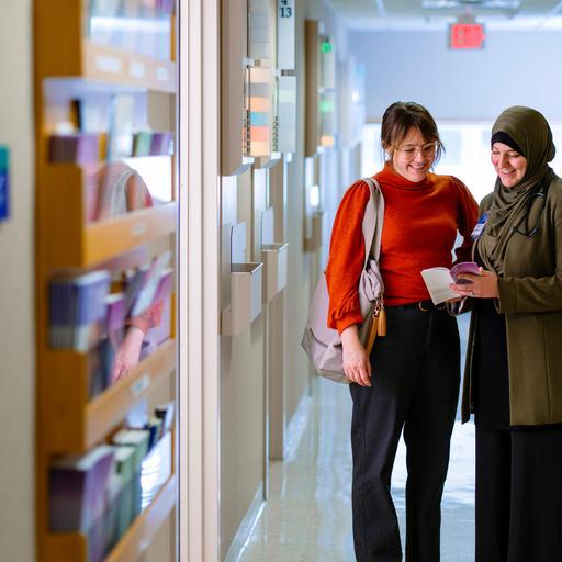 A doctor and patient stand side by side in a hallway and review a medical pamphlet.
