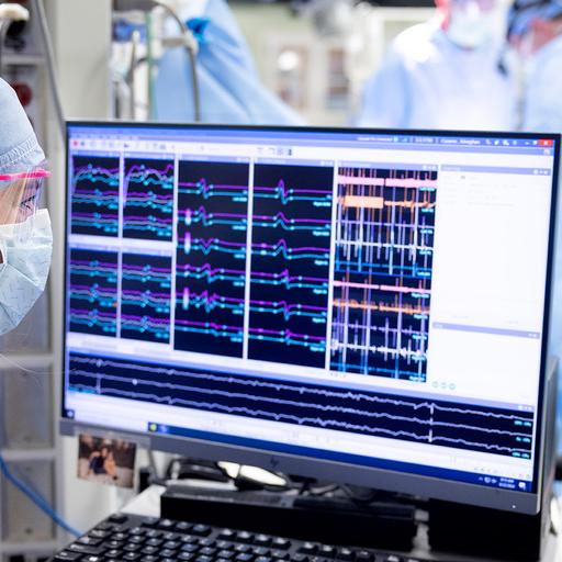 Mayo Clinic professional monitors a screen with patient information on it, while a healthcare team can be seen working on the patient in the background.