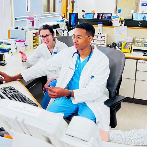 Three doctors are in an office sitting at a desk having a discussion while looking at a computer monitor.