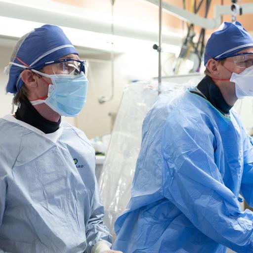 Two doctors wearing medical scrubs in an operating room performing a procedure.
