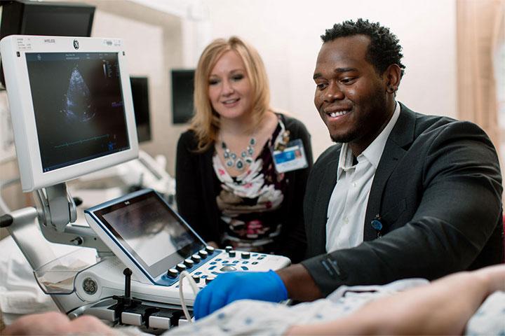 Student and faculty member in an exam room performing a cardiac sonography on a test patient