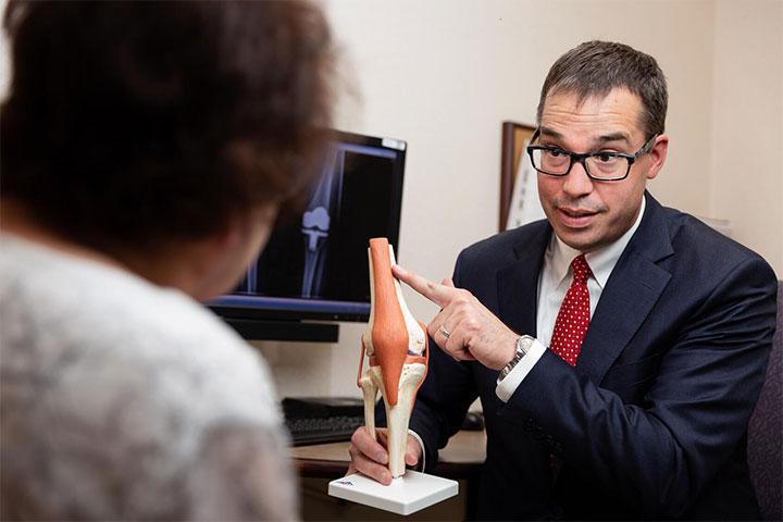 Tad Mabry, M.D., speaks with a patient while holding a model of a knee in an exam room at Mayo Clinic in Rochester, Minnesota.