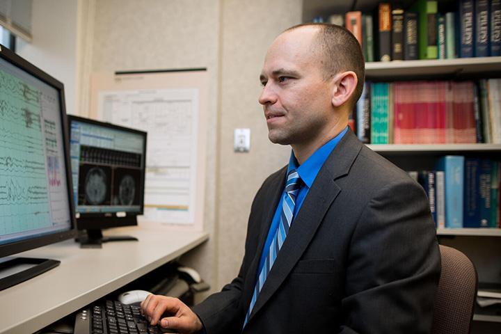 Brian Lundstrom, M.D., Ph.D. at a computer desk looking at a computer monitor.