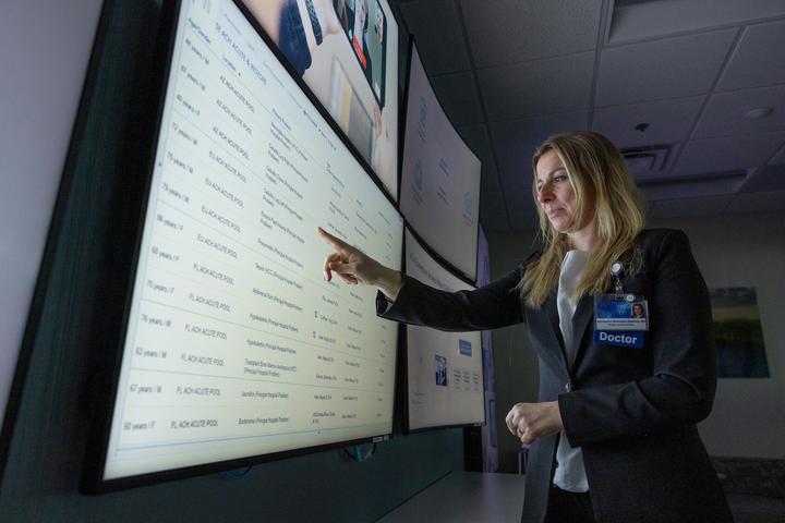 Aleksandra Murawska Baptista, MD, Hospital Internal Medicine Consultant, looks at information on a large screen in the Advanced Care at Home (ACH) command center in Jacksonville, Florida.