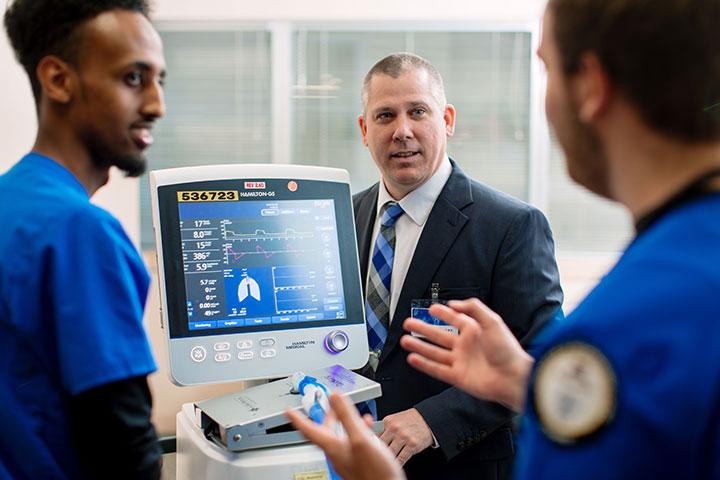Students and faculty standing around computer monitor explaining content on screen