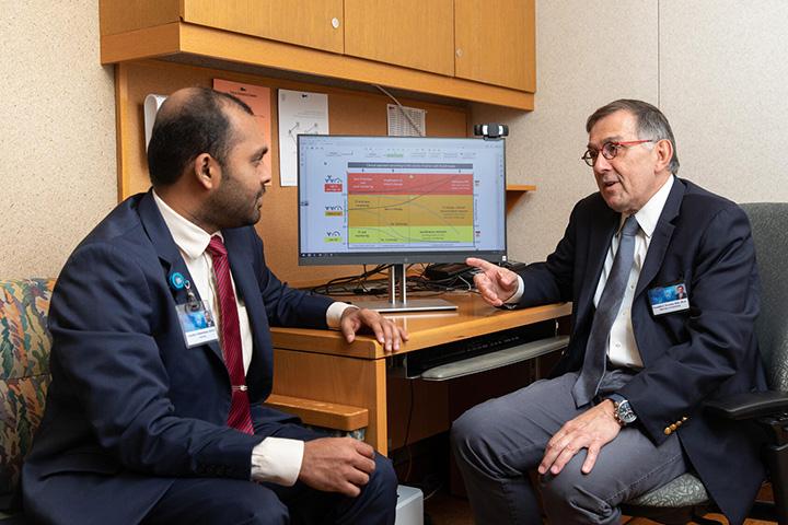 Two doctors in an office sitting at a desk and having a discussion.