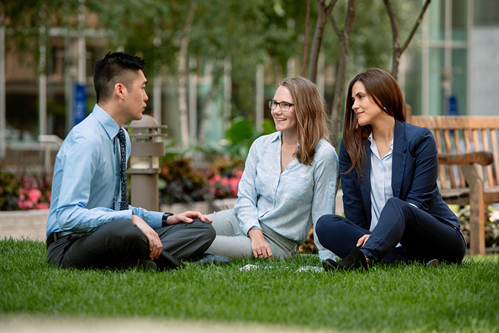 Ph.D. students sit in the grass on campus at Mayo Clinic and visit with each other